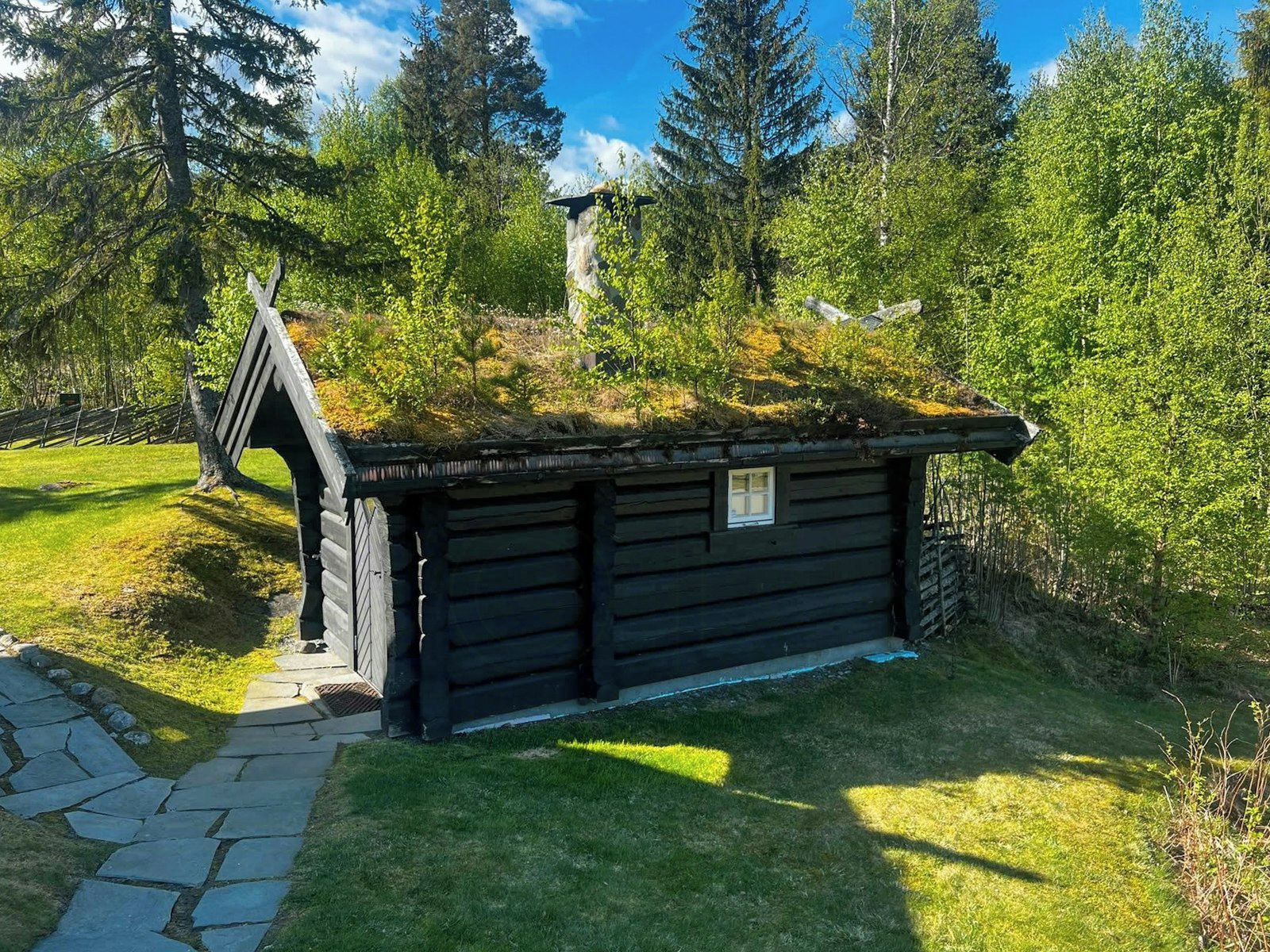 A wooden cabin with a sloped roof, surrounded by lush greenery and trees.
