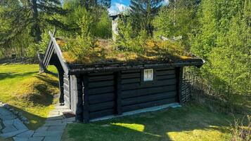 A wooden cabin with a sloped roof, surrounded by lush greenery and trees.