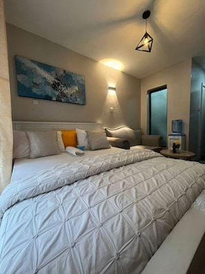 A hotel room with a large bed, a wall-mounted light, a painting, and a water dispenser. - Serene bed sitter apartment in the heart of Nairobi, private and cozy (Nairobi)