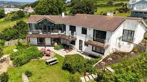 A modern two-story house with a large balcony, a garden with a wooden bench, and a view of the surrounding landscape. - Little Acres - sleeps 12 guests  in 5 bedrooms (Marazion)