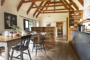 A spacious kitchen with wooden beams, a dining area with chairs, and a view of the adjacent living room. - Mowhay Barn - sleeps 6 guests  in 3 bedrooms (Helford)