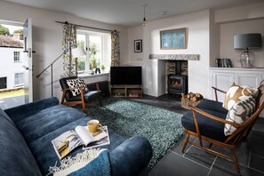 Ein Wohnzimmer mit Sofa, Sesseln, Kamin, Fernseher und Blick ins Freie.