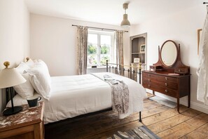 Ein Schlafzimmer mit Bett, Nachttisch, Lampe, Kommode, Spiegel, Fenster und Vorhängen.