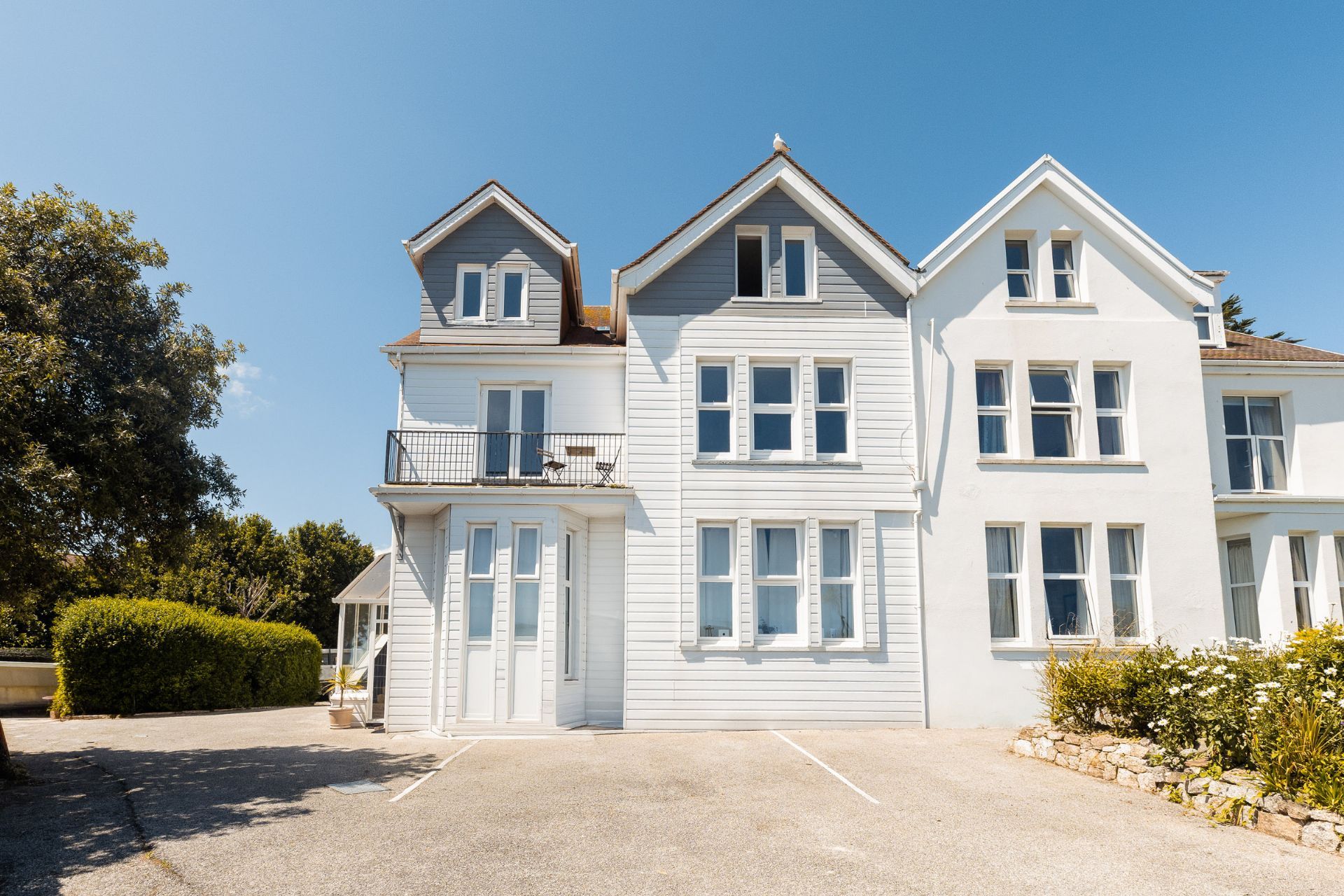 A two-story building with a balcony on the second floor, a driveway, and a garden area.