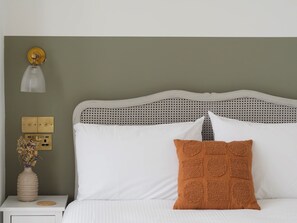 A bed with a white headboard, a single orange pillow, and a white bedside table with a vase of dried flowers. - Seashells Apartment - sleeps 2 guests  in 1 bedroom (Falmouth)