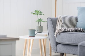 A room with a grey sofa, a small round table with a mug, and a potted plant. - Skylark Beach House - sleeps 6 guests  in 3 bedrooms (Hayle)