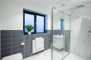 Une salle de bain moderne avec une douche à parois de verre, des toilettes blanches, un lavabo et une fenêtre agrémentée d’une plante.