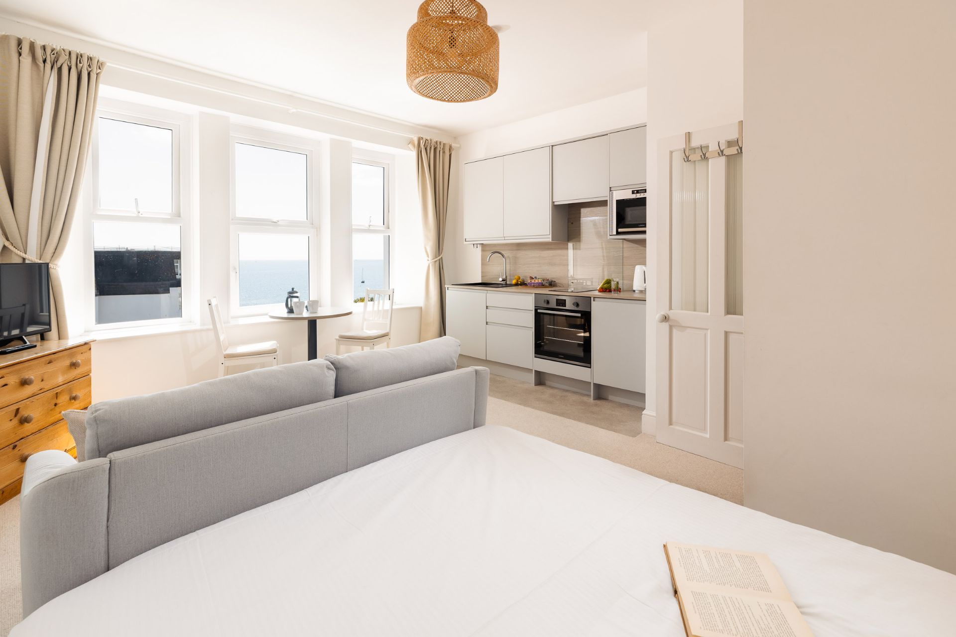 A modern bedroom with a large bed, a television, and a view of the sea through the windows.