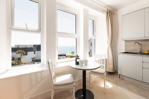 A modern kitchen with white cabinets, a round table, and a view of the sea. - Starfish Studio Apartment - sleeps 2 guests  in 1 bedroom (Falmouth)