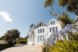 Een herenhuis met balkon, omgeven door weelderige begroeiing en bloeiende planten.
