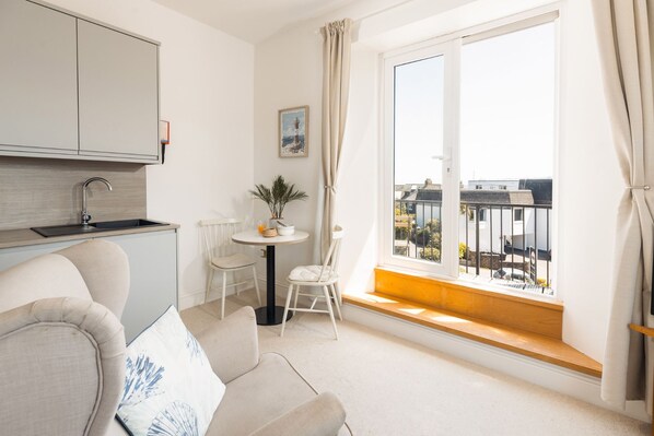 Ein modernes Apartment mit Küchenzeile, einem Essbereich mit Tisch und Stühlen sowie einem großen Fenster mit Blick auf die Umgebung.