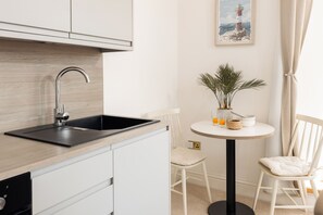 A modern kitchen with a black sink, white cabinets, and a round table with a plant. - Sunrise Studio Apartment - sleeps 2 guests  in 1 bedroom (Falmouth)