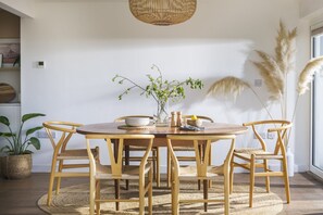 A round wooden dining table with six chairs, a woven rug, and a hanging light fixture. - Sunset Sands - sleeps 8 guests  in 4 bedrooms (Newquay)