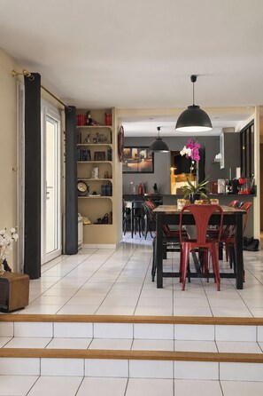 A dining area with a table and chairs, a bookshelf, and a kitchen in the background. - House with a private pool – sleeps 6 (Châteauneuf-de-Gadagne)