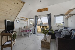 A cozy living room with a flat-screen TV, white chairs, a wooden coffee table, and a sofa with patterned cushions. - Seamist  - sleeps 2 guests  in 1 bedroom (Hayle)