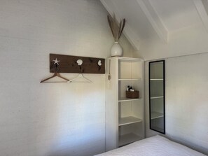 A bedroom with a bed, a wardrobe, a mirror, and a wall-mounted shelf with decorative items. - The Grevelingenmeer Beach House | Peace, romance, nature, and water (Herkingen)