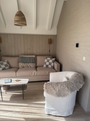 A modern living room with a beige sofa, a white armchair, a woven pendant light, and a small table with a notebook and coins. - The Grevelingenmeer Beach House | Peace, romance, nature, and water (Herkingen)