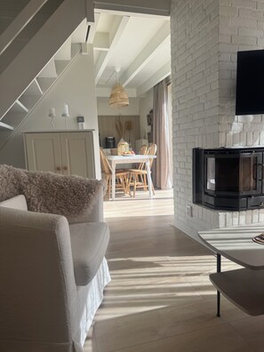 A modern living room with a sofa, a dining area with chairs, a staircase, and a fireplace. - The Grevelingenmeer Beach House | Peace, romance, nature, and water (Herkingen)
