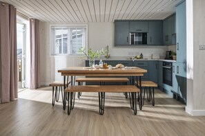 A modern kitchen with a wooden table and benches, a microwave, and a stove. - Spindrift - sleeps 6 guests  in 3 bedrooms (Hayle)