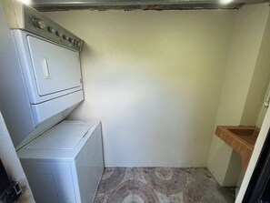 Une buanderie équipée d’un lave-linge et d’un sèche-linge superposés, d’une petite étagère en bois et d’un sol carrelé.