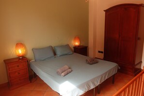 A bedroom with a bed, two nightstands, a wooden wardrobe, and a tiled floor. - Vrbo Property (Carruba-San Leonardello)