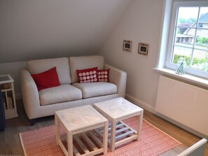 Ein Wohnzimmer mit einer Couch, zwei kleinen Tischen, einem gemusterten Teppich und einem Fenster mit Aussicht.