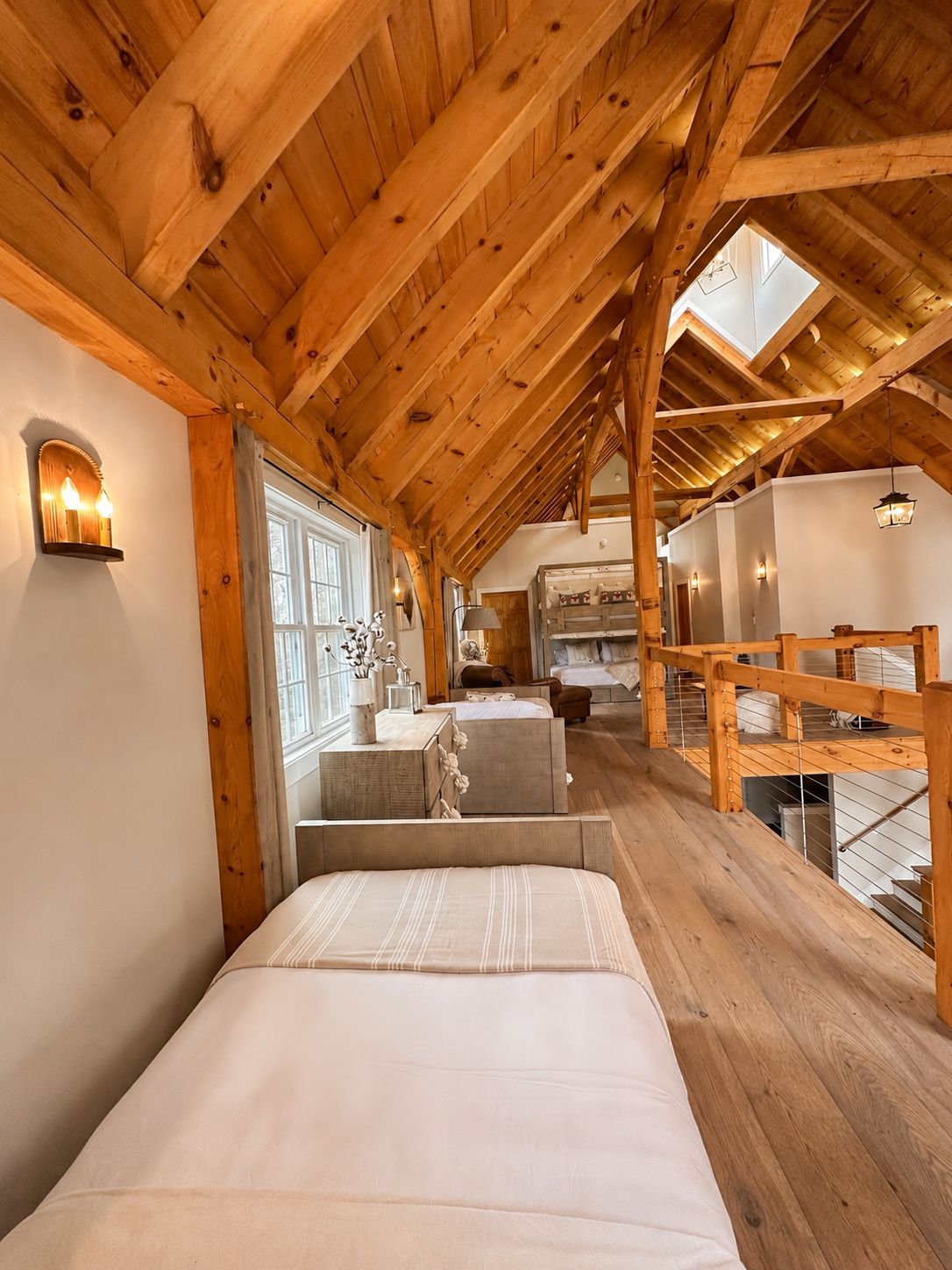 A high-ceilinged room with wooden beams, a bed, a desk, and a window.