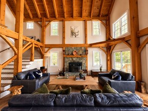 Una sala de estar amplia con chimenea de piedra, vigas de madera y ventanas grandes.