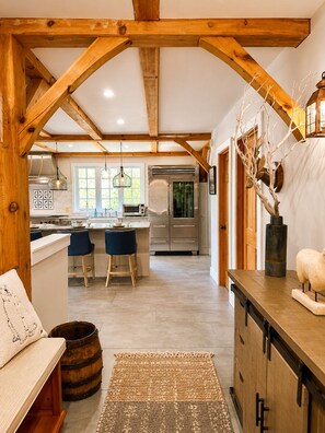 A kitchen with wooden beams, a refrigerator, and a dining area with stools. - Mount Snow Retreat | Hot Tub, Sauna & Game Room (West Dover)