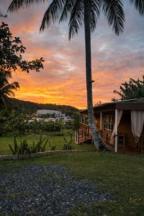 Ein tropisches Resort mit einer Palme, einem Holzgebäude mit Veranda und Blick auf ein entferntes Gebäude.