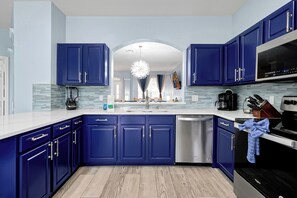 A modern kitchen with blue cabinets, a dishwasher, a coffee maker, and a microwave. - Themed 6BR Arcade Home w/ Private Pool & Spa near Disney (Kissimmee)