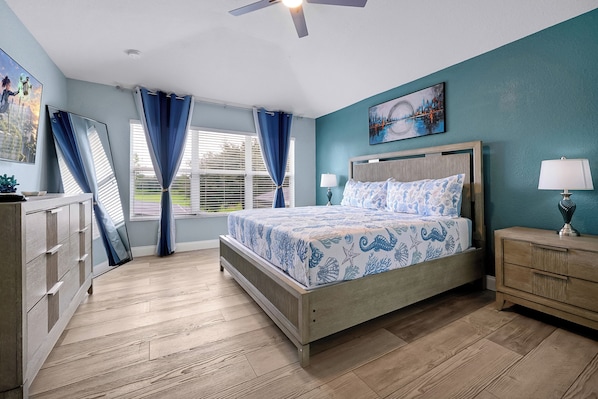 Un dormitorio con cama, mesita de noche, cómoda, ventana con cortinas y ventilador de techo.