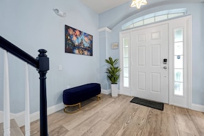 A hallway with a wooden floor, a white door with a glass panel, a bench, a potted plant, and a painting on the wall. - Themed 6BR Arcade Home w/ Private Pool & Spa near Disney (Kissimmee)