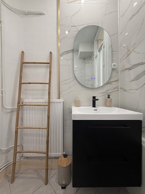 A bathroom with a white sink, black vanity, a mirror, and a wooden ladder. - Vrbo Property (Béziers)