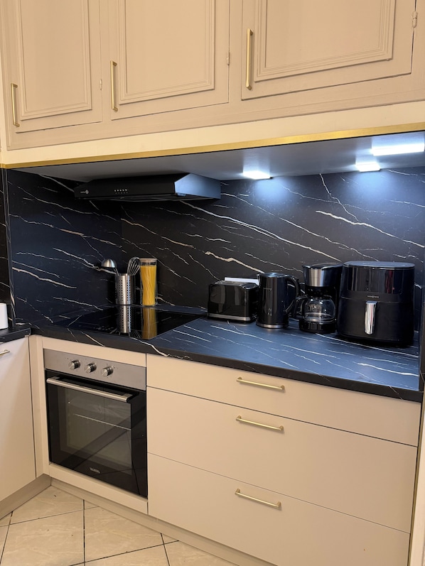 A kitchen with a black marble countertop, stainless steel appliances, and light-colored cabinetry. - Vrbo Property (Béziers)