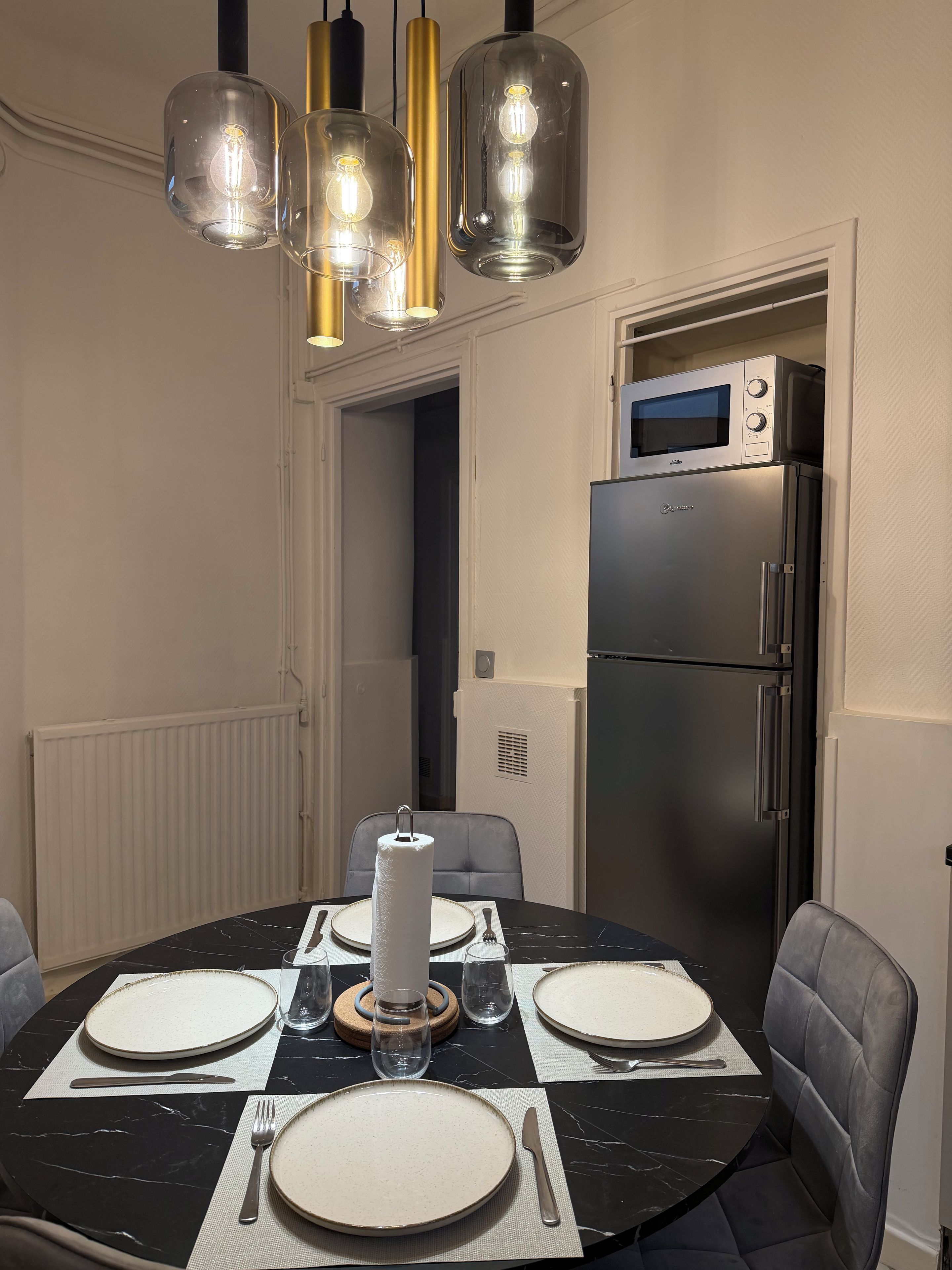 Een eetgedeelte met een ronde tafel voor vier personen, een moderne koelkast en hanglampen.