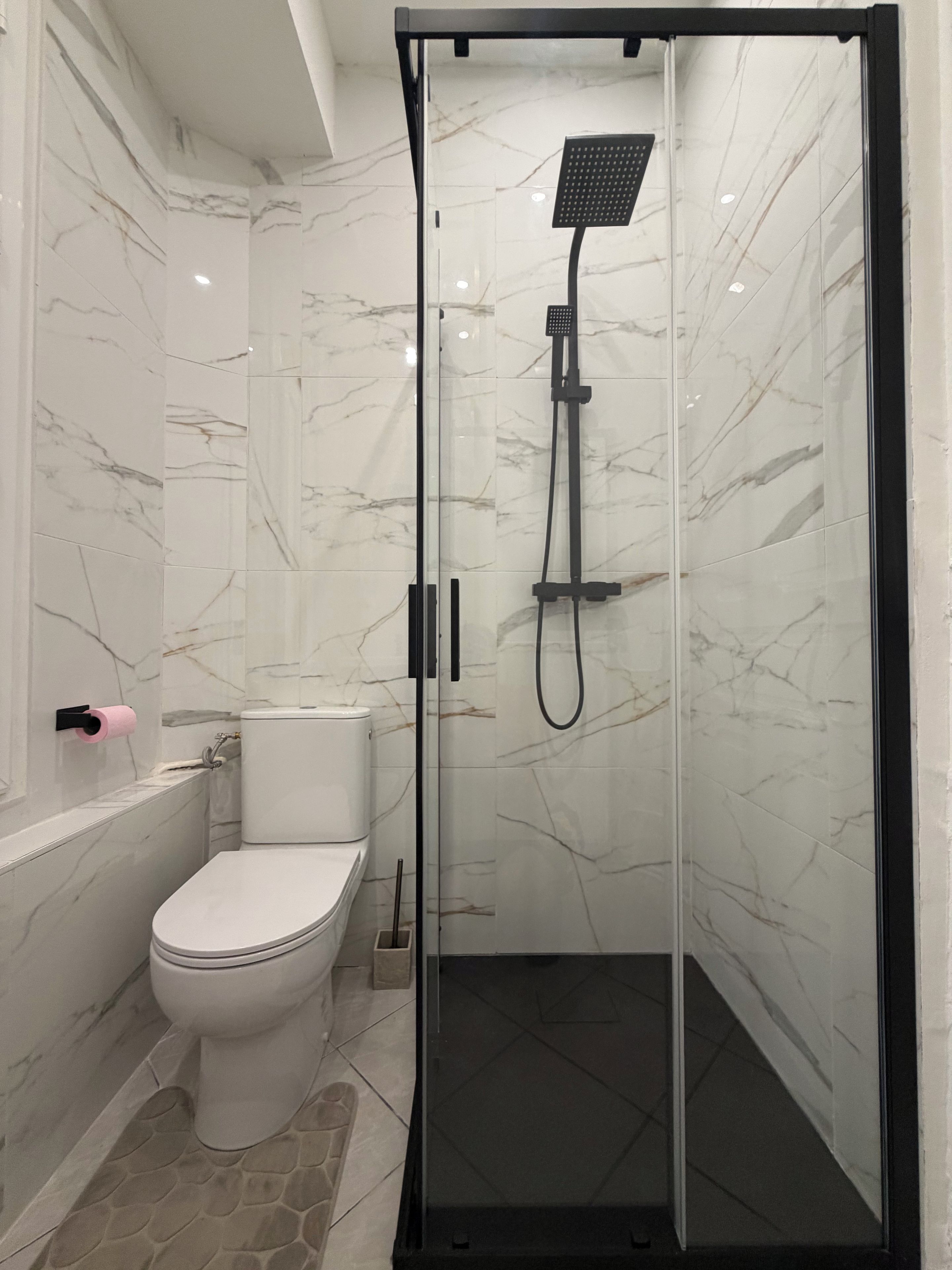 Un baño moderno con ducha envuelta en vidrio, inodoro y pared con azulejos de mármol.