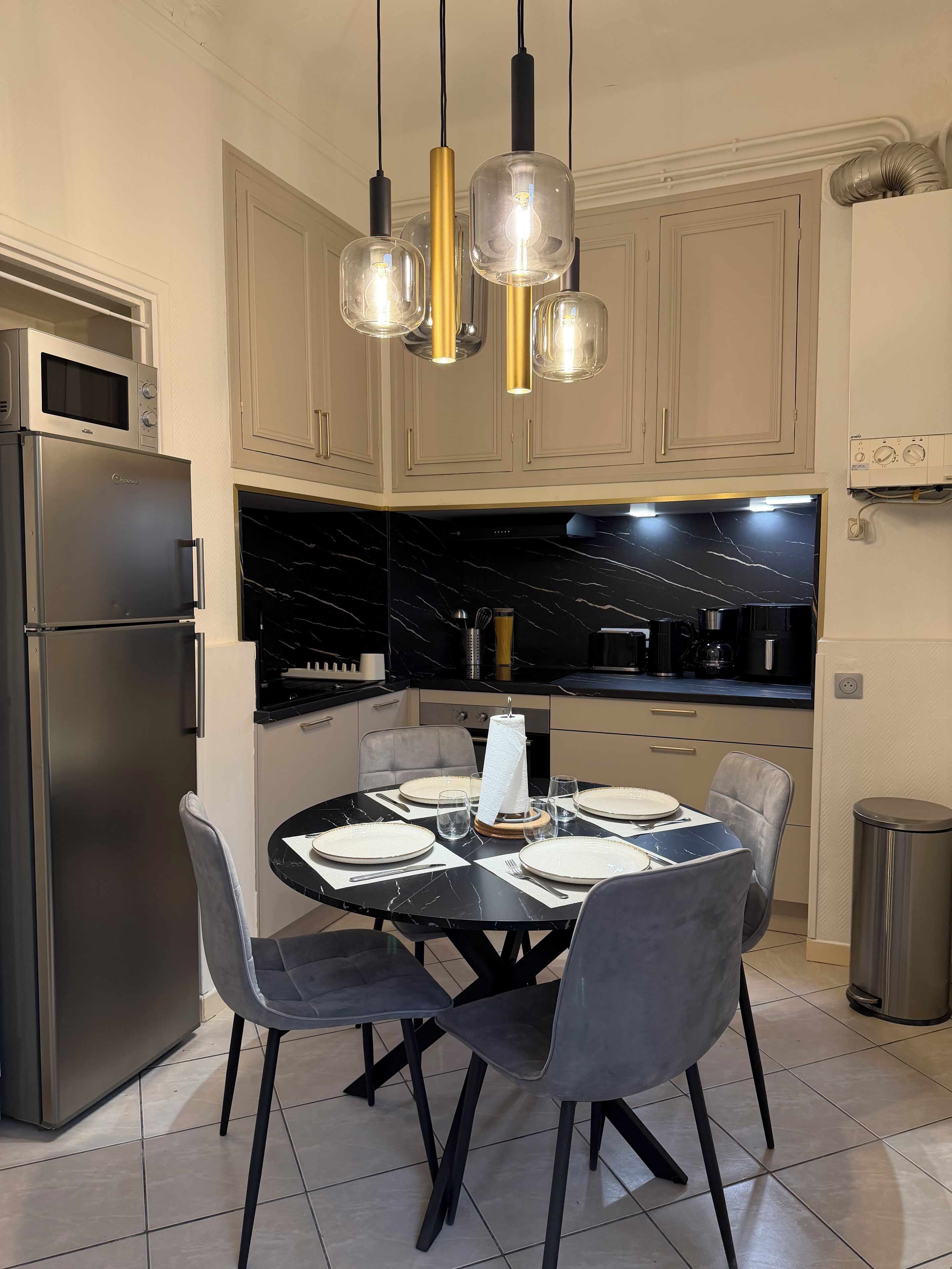 Une cuisine moderne dotée d’un four encastré, d’une table à manger pour quatre personnes et de luminaires suspendus.