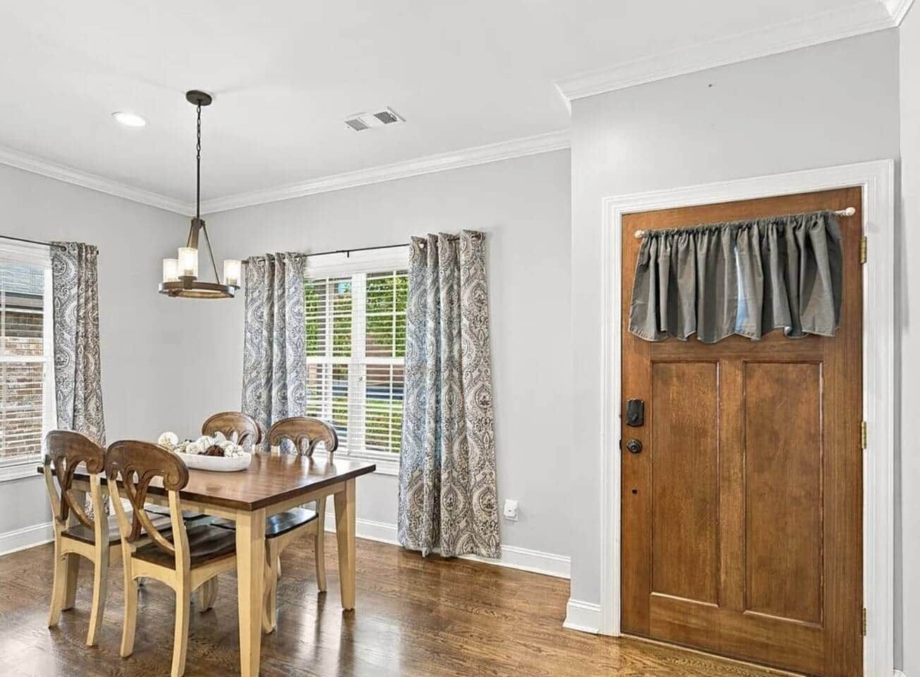 Un'area pranzo con tavolo e sedie in legno, un lampadario e tende a motivi decorativi.