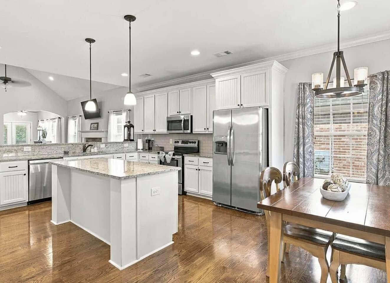A modern kitchen with white cabinetry, stainless steel appliances, and a wooden dining table.