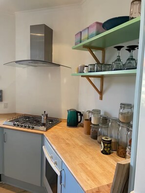 Une cuisine équipée d’une cuisinière à gaz, d’une hotte en acier inoxydable, d’un plan de travail en bois et de divers ustensiles de cuisine, comme des bocaux et une bouilloire.