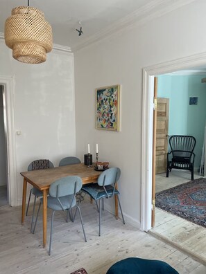 Un coin repas avec une table en bois, quatre chaises, un luminaire suspendu et un tableau au mur.