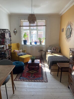 Un salon chaleureux avec un fauteuil jaune, un canapé, une table basse et un tapis à motifs.