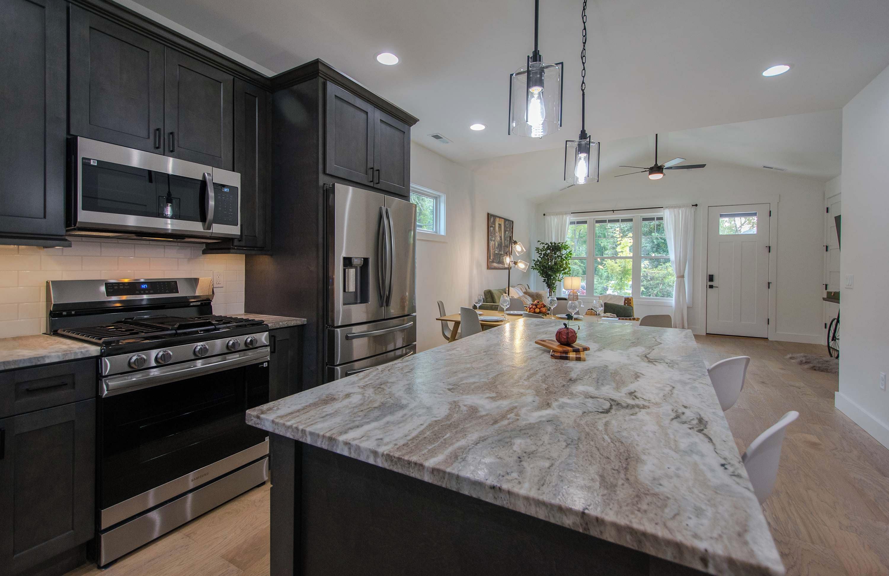 A modern kitchen with dark cabinetry, stainless steel appliances, and a marble island.