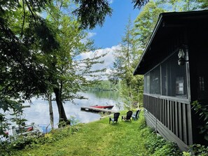 A lakeside cabin with a dock, chairs, and a boat. - Lake Fairlee Waterfront Cottage with Screened Sleeping Porch & Beautiful Views (Fairlee)