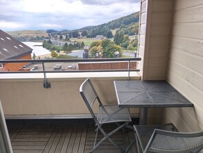 A balcony with a table and chairs, overlooking a river and a hilly landscape. - Charming bright apartment - 8 guests (Besse-et-Saint-Anastaise-Super Besse)