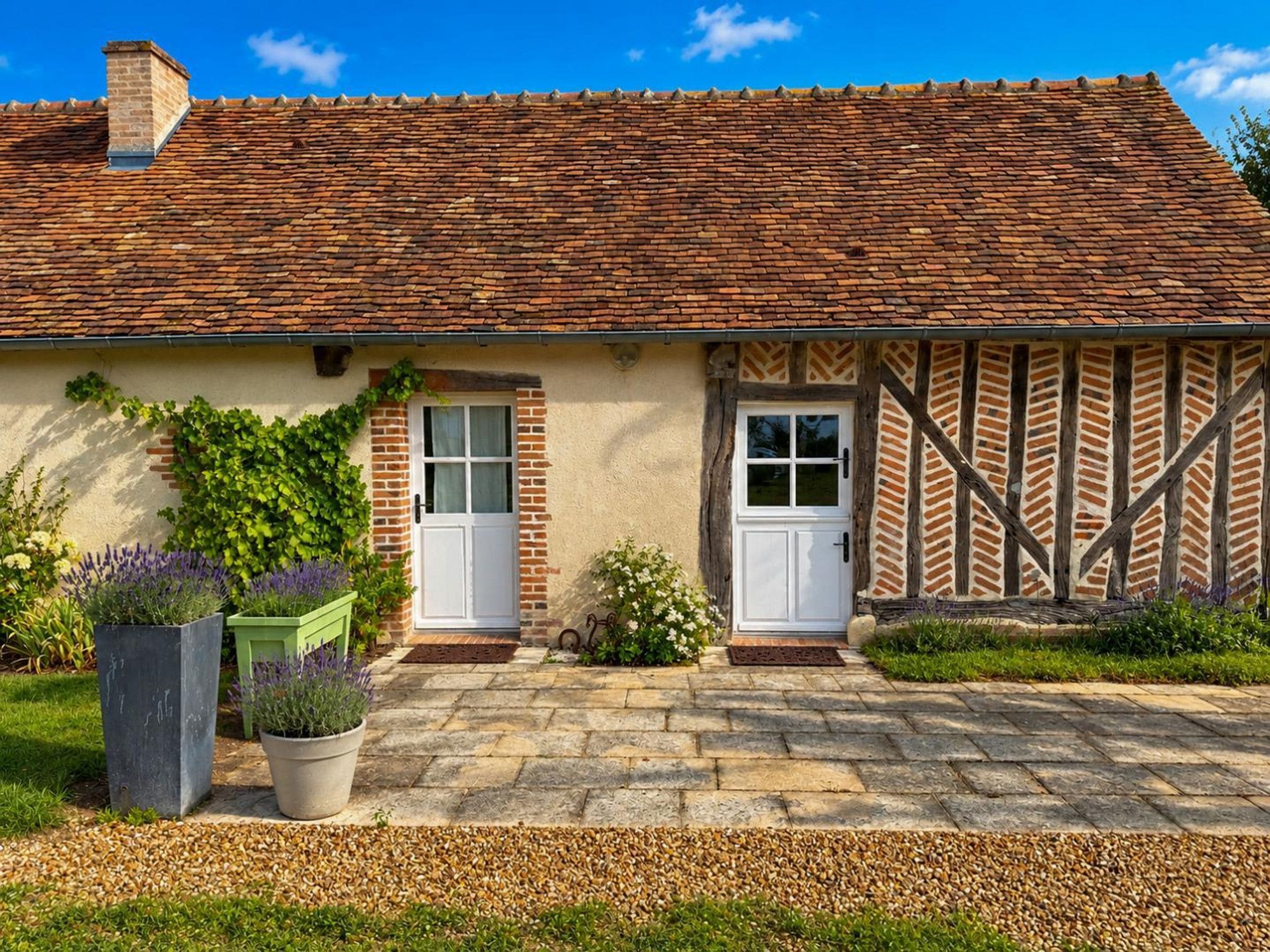 A traditional brick house with a tiled roof, two white doors, and a stone pathway leading to the entrance.