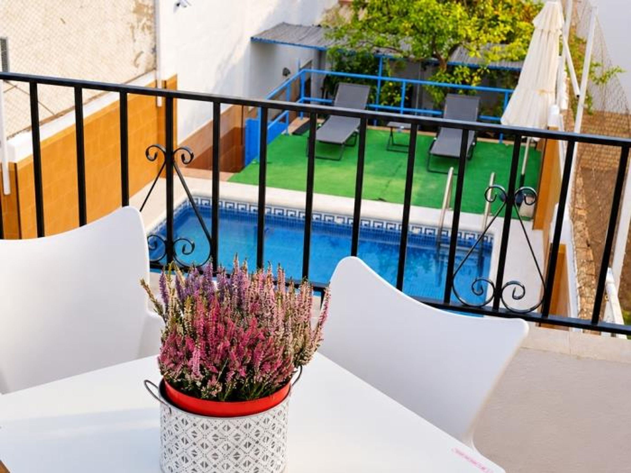 Ein Balkon mit weißem Tisch, einem Blumentopf und Blick auf Pool und Garten.