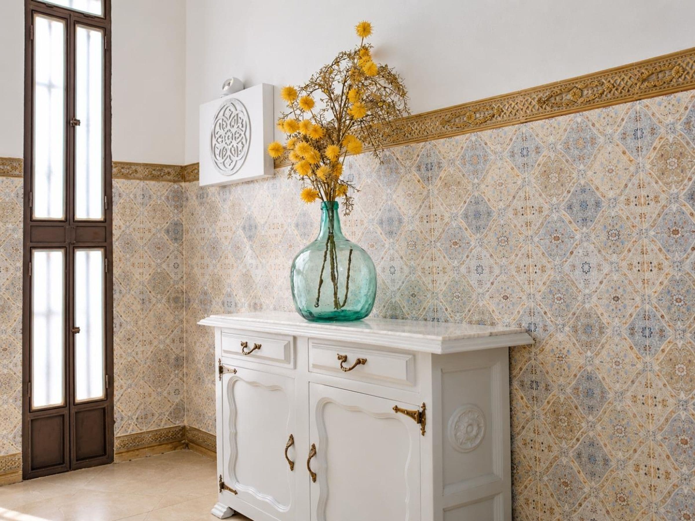 Una habitación con un armario blanco, un jarrón con flores amarillas y baldosas de pared con diseños.