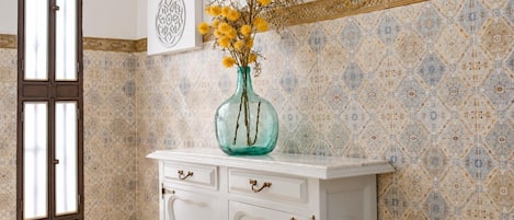 Una habitación con un armario blanco, un jarrón con flores amarillas y baldosas de pared con diseños.